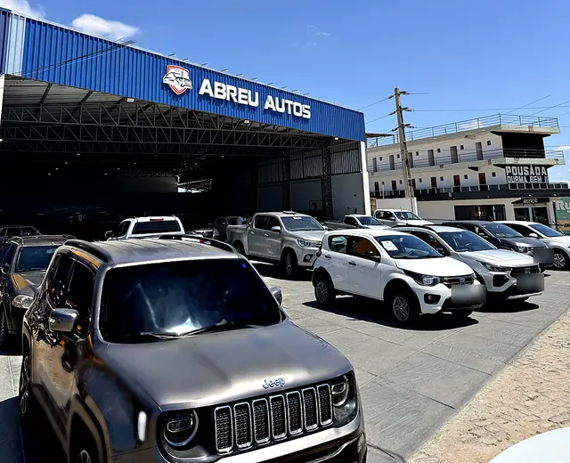 Pátio externo da Abreu Autos com SUVs e picapes em frente ao galpão azul