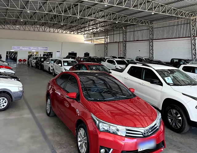 Sedã vermelho em primeiro plano no salão com carros enfileirados